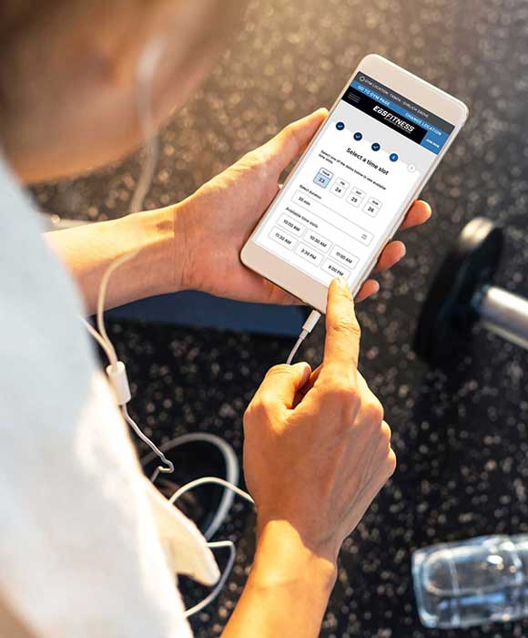 Young woman at the gym on her phone, checking on her child in the gym's childcare center