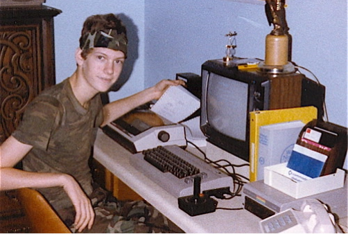 An image that appears to be from the 80s, featuring a teenage boy sitting next to a brick of a computer.