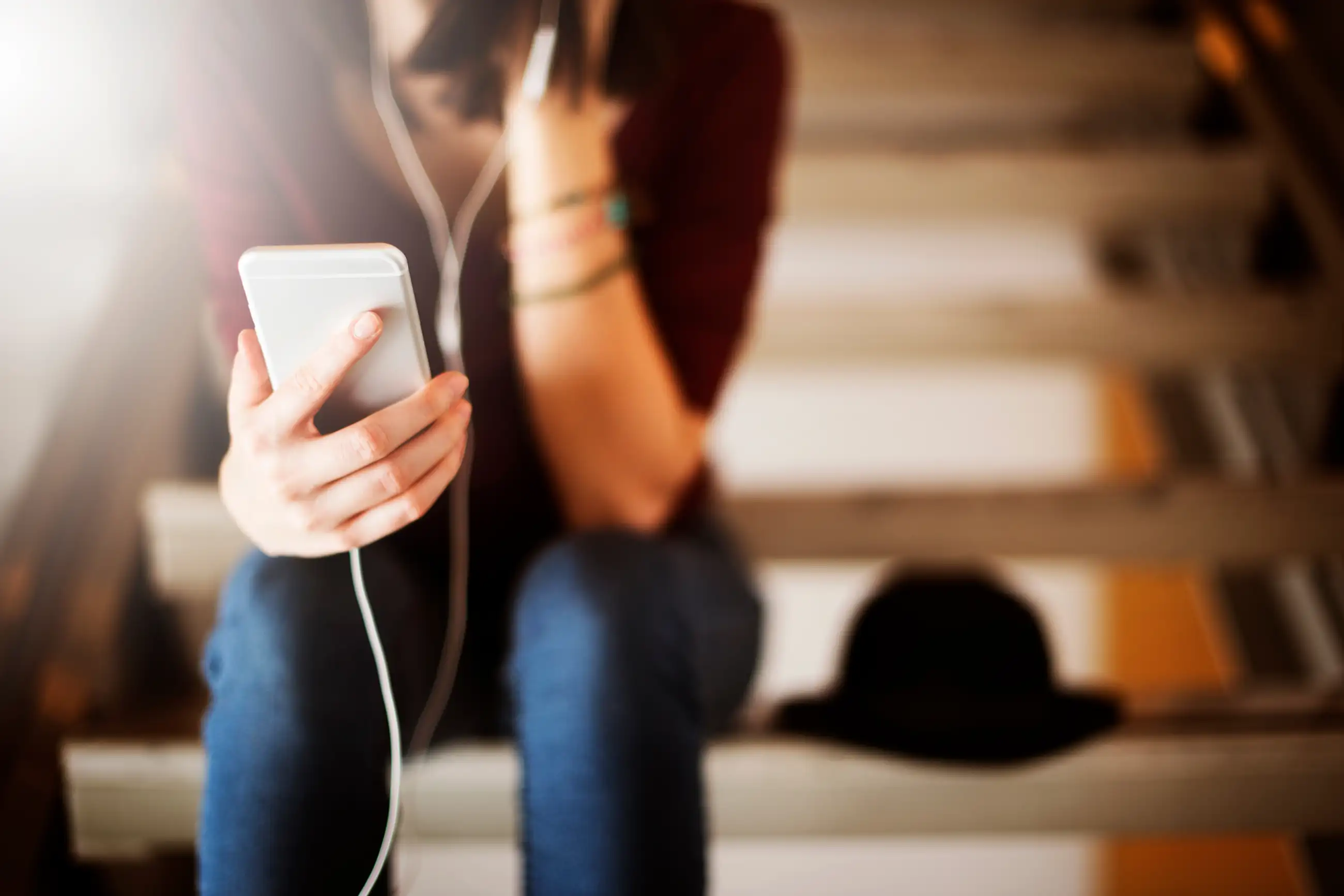 A person sitting on a staircase listening to a podcast on their phone through their headphones.