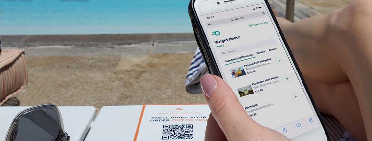 Woman ordering a drink from her phone, lounging by a resort pool.