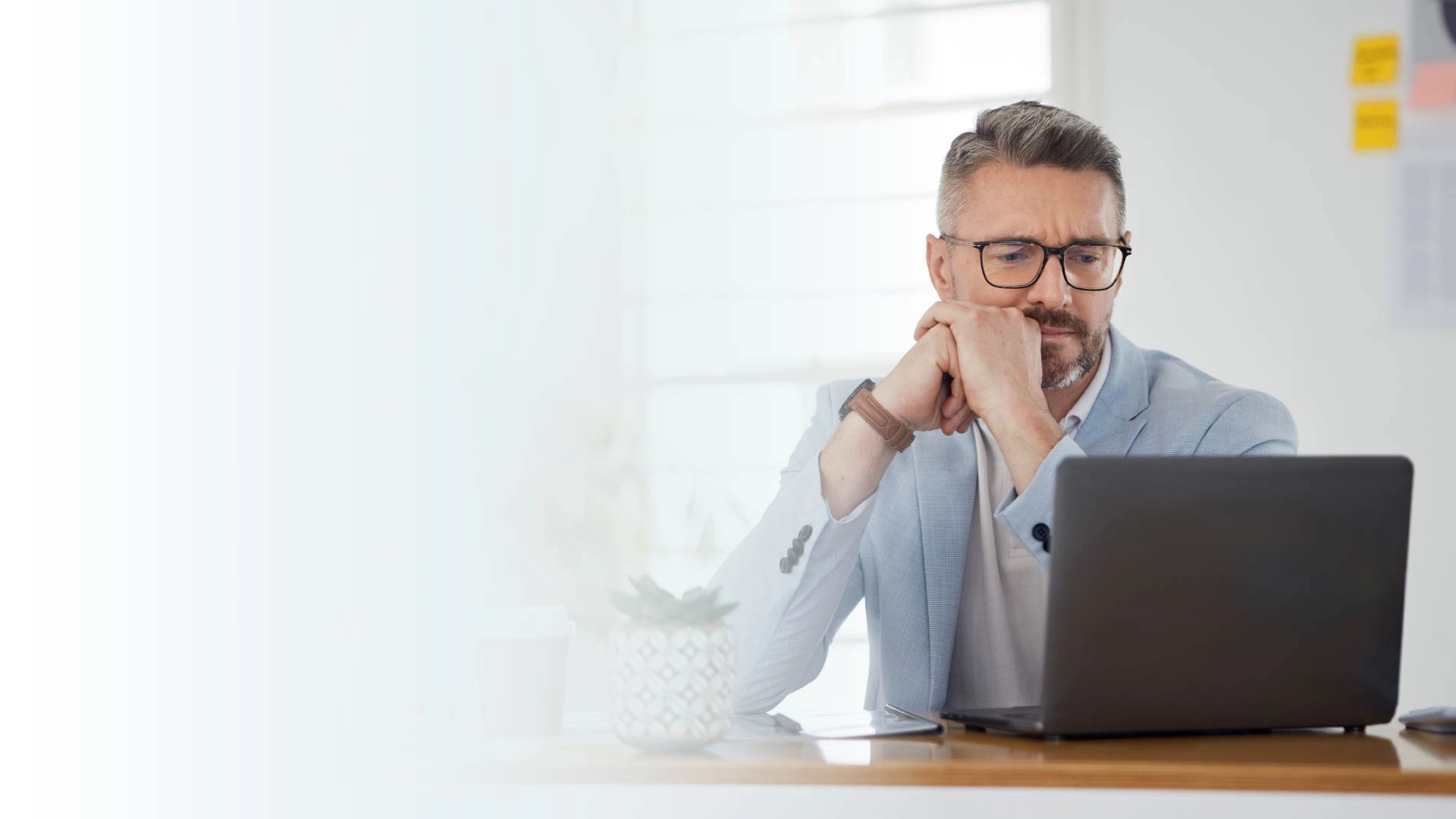 A man sitting at a desk and thinking in front of a laptop